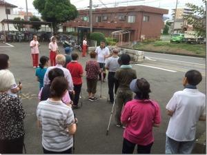 駐車場で指導者の周りに参加者の方々が集まって話を聞いている写真